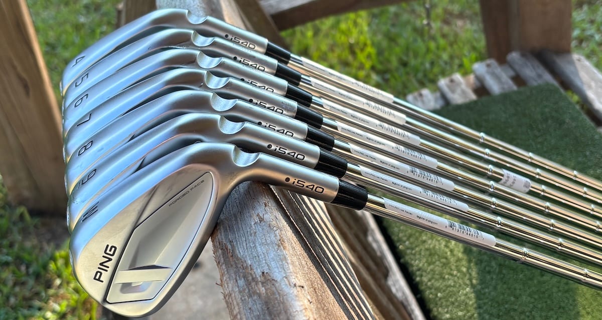 Ping i540 irons set leaning on a rail at the range